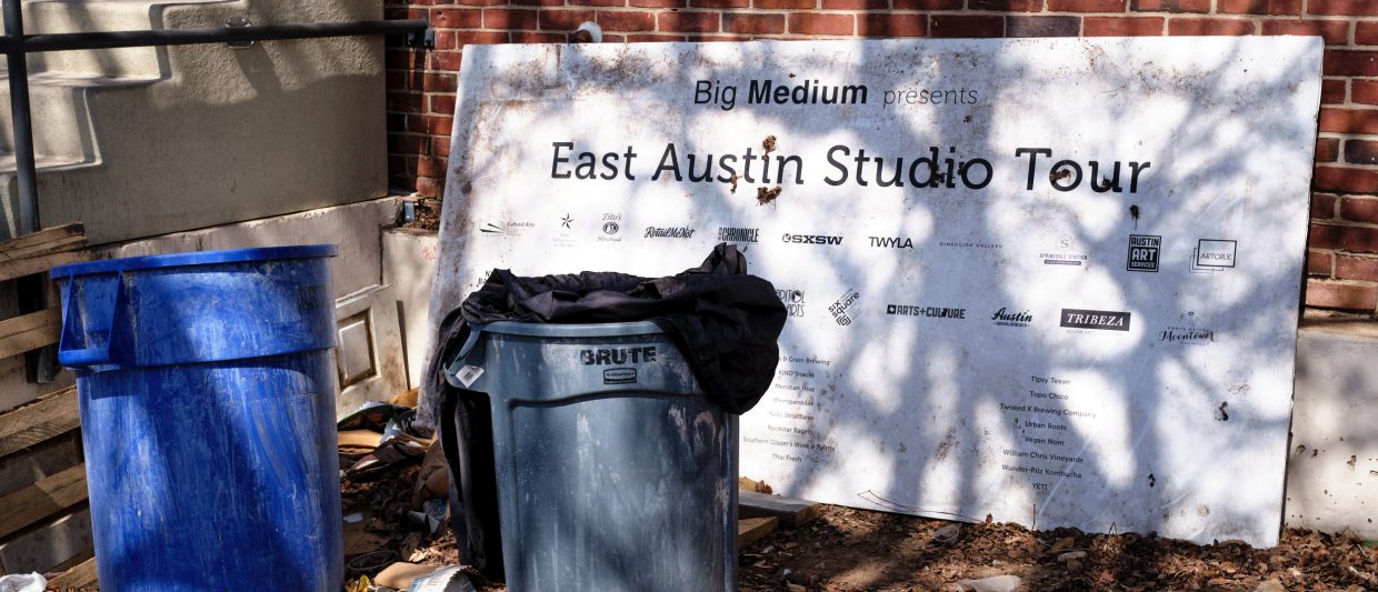 A sign announcing the East Austin Studio Tour set by trash cans.