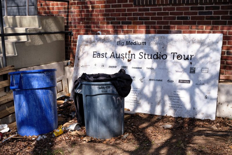 A sign announcing the East Austin Studio Tour set by trash cans.